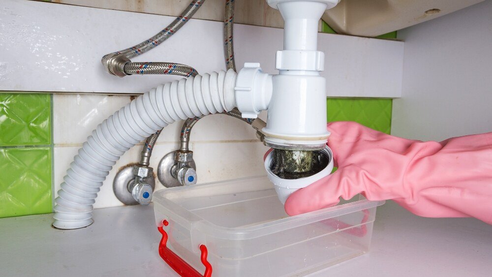 ATC Plumbing technician cleaning out a clogged bathroom sink drain with a container underneath in LA County.