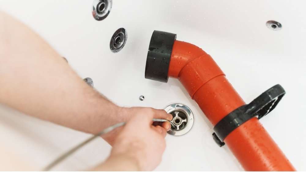 An ATC Plumbing plumber using a cable auger for emergency drain unblocking in a bathtub in LA County.