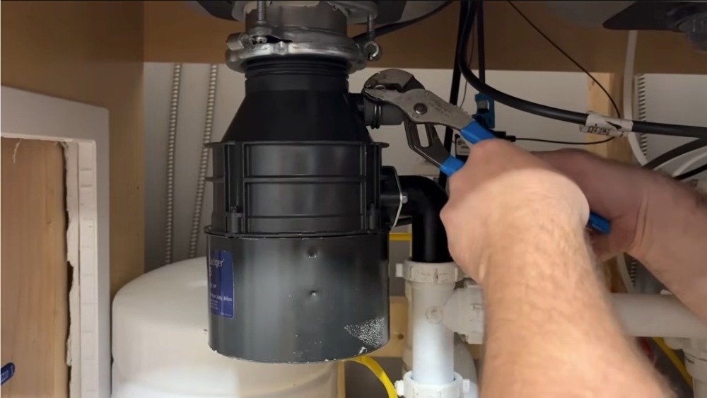 A plumber in Los Angeles performing a garbage disposal repair, using a wrench to fix a leaky unit under a kitchen sink.