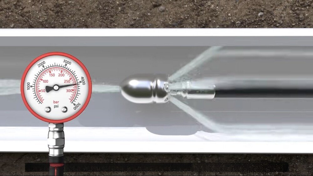 Close-up of a hydro jet nozzle inside a sewer line, with a pressure gauge measuring the high-pressure water used to clean the pipe.