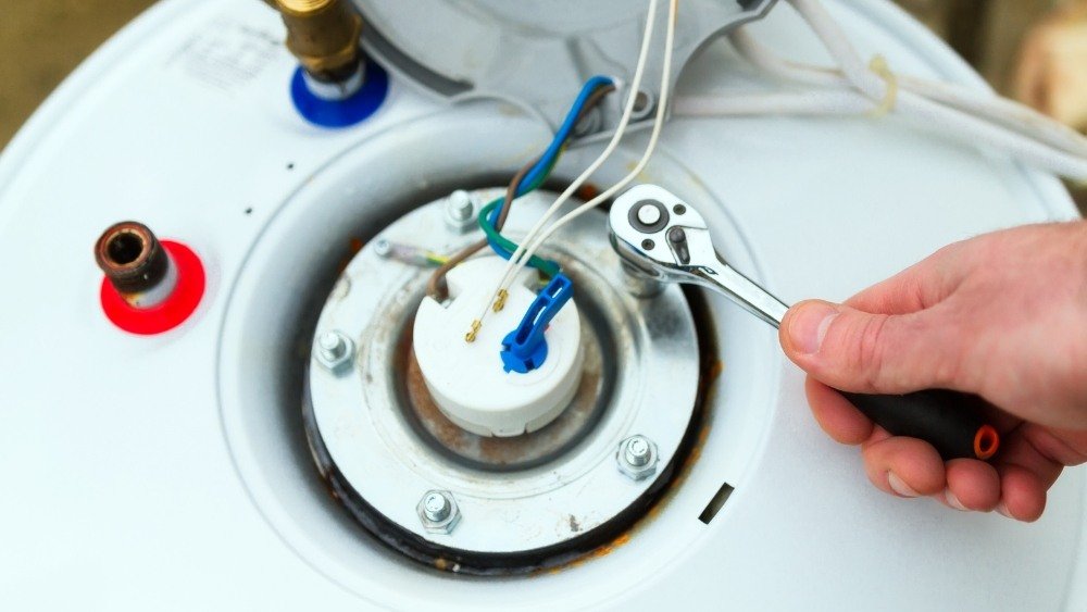 ATC plumbing technician in LA County repairing tankless water heater wiring with tools.