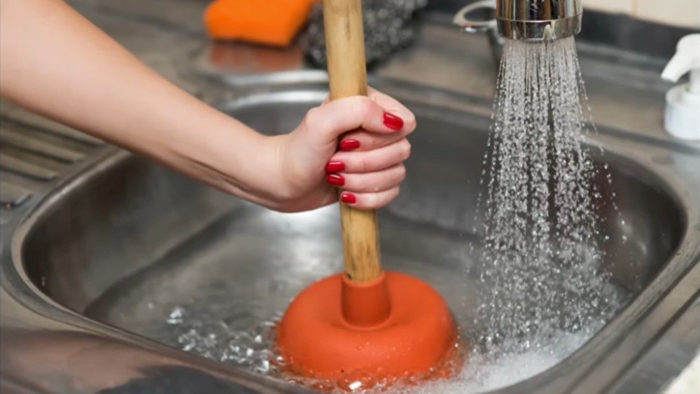 LA Plumber using a plunger to unclog a kitchen sink with a clogged garbage disposal.